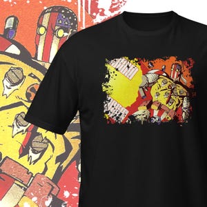 May include: Black t-shirt featuring a graphic print of a comic book character wearing a red, white and blue helmet and a yellow and red suit. The character is holding a weapon and has a determined expression on his face. The graphic is surrounded by a yellow and red splatter effect.