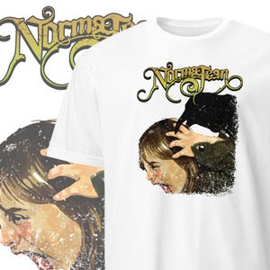 Op de afbeelding: Wit T-shirt met een verweerde afbeelding van een meisje met een raaf op haar hoofd. De raaf is zwart en het meisje heeft bruin haar en schreeuwt. De tekst "Norcross Jean" staat in een gestileerd lettertype boven de afbeelding.