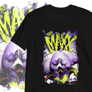 以下が含まれることがあります： 黄色のマスクをした紫色のキャラクターのグラフィックプリントが施された黒いTシャツ。シャツには「The Maxx」という文字が黄色と緑で書かれています。