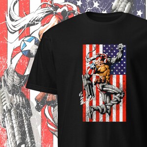 May include: Black t-shirt featuring a graphic of a superhero in a red, white and blue costume standing in front of an American flag.