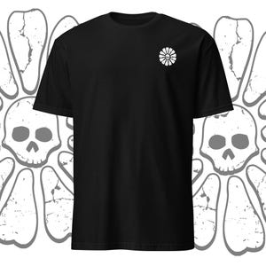 Peut inclure: T-shirt noir avec un motif de marguerite blanche sur la poitrine gauche. La marguerite a un crâne au centre.