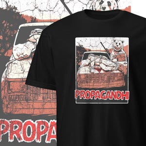 May include: Black t-shirt with a distressed graphic of a person tied to the hood of a car with a bear standing behind them. The text "PROPAGANDHI" is printed below the graphic.