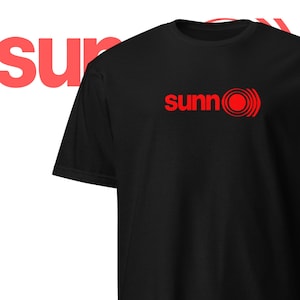 以下が含まれることがあります： 赤いロゴが「sunn0」と書いてある黒いTシャツ。赤い円と、その中に同心円が描かれている。