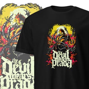 Könnte beinhalten: Schwarzes T-Shirt mit einem Grafikdruck eines Comic-Charakters mit gelber Haut und roten Haaren, umgeben von mechanischen Tentakeln. Der Charakter trägt ein schwarzes Shirt und eine schwarze Hose. Der Text "The Devil Wears Prada" ist in einer stilisierten Schrift unter dem Charakter geschrieben.