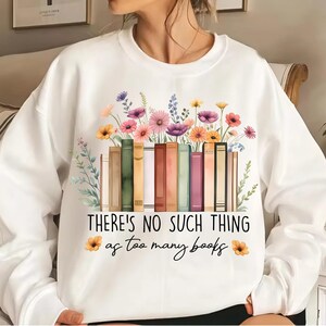 May include: White sweatshirt featuring a graphic of a stack of books with flowers on top. The text "There's no such thing as too many books" is printed below the graphic.