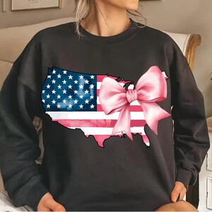 May include: Black sweatshirt featuring a graphic of the United States map in the shape of an American flag with a pink bow on top.