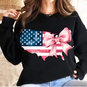May include: Black sweatshirt featuring a graphic of the United States map outlined in black with a pink bow and an American flag design.
