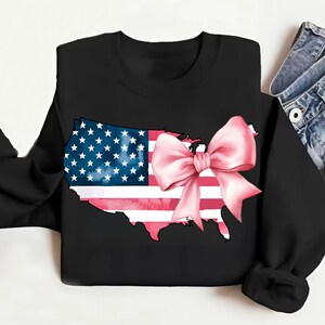 May include: Black sweatshirt featuring a pink bow on a watercolour outline of the United States of America. The American flag is inside the outline.