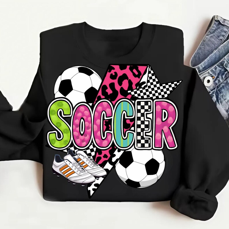 Puede incluir: Sudadera negra con un dise&ntilde;o gr&aacute;fico de un bal&oacute;n de f&uacute;tbol, botas de f&uacute;tbol y la palabra "SOCCER" en letras de colores con estampado de leopardo y patr&oacute;n a cuadros.