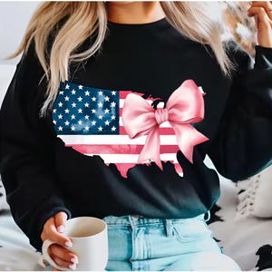 May include: Black sweatshirt featuring a graphic of the United States outline in the shape of an American flag with a pink bow on top.