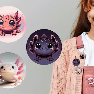 Könnte beinhalten: Drei bunte Axolotl-Anstecker mit verschiedenen Designs. Die Anstecker zeigen einen rosa Axolotl mit roten Kiemen, einen schwarzen Axolotl mit weißen Flecken und einen weißen Axolotl mit rosa Kiemen. Die Anstecker sind an einem rosa Pullover befestigt.