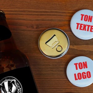 May include: A brown beer bottle with a black label featuring a badger logo, a gold bottle opener, and two white buttons with red text that reads "TON TEXTE" and "TON LOGO".