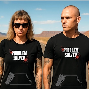Può includere: T-shirt nere con la scritta bianca "PROBLEM SOLVED", con spruzzi rossi. Le magliette presentano anche una grafica di una pistola in un design a tasca. L'immagine mostra due persone che indossano le magliette.