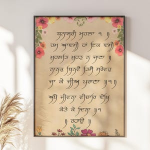 May include: A rectangular wall art print featuring black Gurmukhi script centered on a light tan background. The border is decorated with colorful floral illustrations in shades of pink, yellow, and green, framing the text in a vertical orientation.