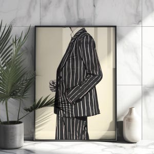 May include: A framed art print featuring a black and white pinstripe suit. The illustration shows a person in a suit, with one hand in a pocket. The artwork is displayed on a marble surface, with a potted plant and a white vase.
