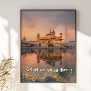 Könnte beinhalten: Ein gerahmter Wandkunstdruck, der den Goldenen Tempel bei Sonnenuntergang zeigt, wobei sich das goldene Bauwerk im ruhigen Wasser spiegelt. Das Bild enthält weißen Text in Gurmukhi-Schrift am unteren Rand vor einem orange-violetten Himmel.