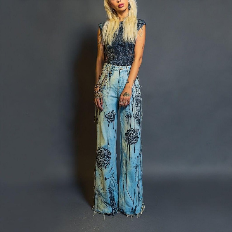K&ouml;nnte beinhalten: Hellblaue Jeans mit weitem Bein, mit schwarzen Rosendesigns und schwarzen Farbtropfen. Die Jeans haben einen ausgefransten Saum und werden mit einem dunkelblauen Oberteil mit Muster kombiniert. Das Outfit ist ein einzigartiger, k&uuml;nstlerischer Stil.