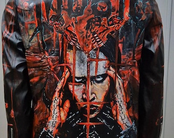 Könnte beinhalten: Schwarze Lederjacke mit auffälligem rot-schwarzem Grafikdesign auf dem Rücken. Das Kunstwerk zeigt ein Porträt mit einer käfigartigen Struktur und aufwendigen Details. Die Jacke hat einen klassischen Kragen und Reißverschlussdetails.