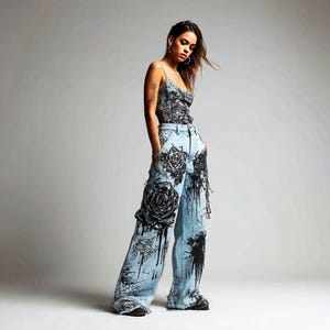 K&ouml;nnte beinhalten: Ein hellblaues Jeans-Outfit mit schwarzem Blumendesign. Das Outfit umfasst ein Camisole-Top und eine weite Jeans mit einer gro&szlig;en Rosengrafik und Farbspritzern. Das Model tr&auml;gt das Outfit.