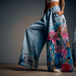 May include: Light blue denim wide-leg trousers with a vibrant floral design. The trousers feature a watercolor-style painting of pink, orange, and white flowers against a blue background. Dark blue paint splatters add detail to the bottom.