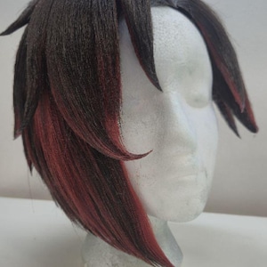 May include: A dark brown wig with red highlights, styled on a mannequin head. The wig features a layered cut with side-swept bangs and red streaks framing the face. The hair is styled to be slightly spiky.