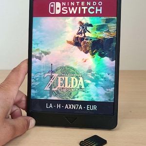 Peut inclure: Un boîtier de jeu Nintendo Switch noir pour The Legend of Zelda: Tears of the Kingdom avec une illustration de paysage fantastique coloré, le titre du jeu et le code LA-H-AXN7A-EUR, accompagné d'une petite cartouche de jeu noire.