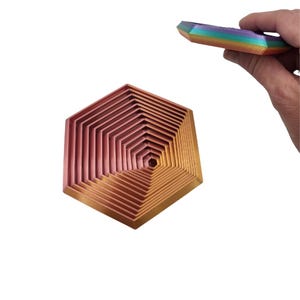 以下が含まれることがあります： バラゴールドと銅のグラデーションで仕上げられた、入れ子になった六角形の金属製のトレイのセット。トレイは互いに積み重ねられており、らせん状の効果を生み出しています。