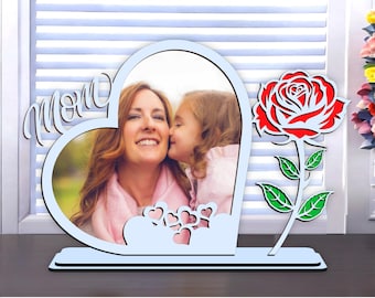 May include: A light blue heart-shaped photo frame with the word "Mom" in cursive. The frame holds a photo of a woman and child. A red and white rose is on the right side. The text "SVG PNG PDF EPS DXF FILES" is at the bottom.