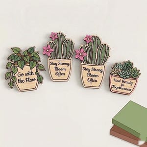 May include: Four wooden plant-themed pins featuring potted greenery. One shows a trailing plant with 'Go with the Flow', two show cacti with pink flowers and 'Stay Strong, Bloom Often', and one shows succulents with 'Find Beauty in Togetherness'.