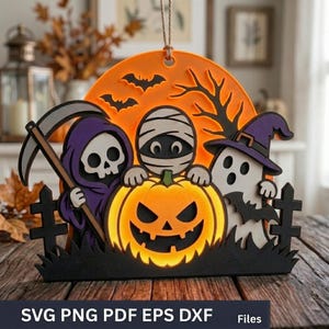 Puede incluir: Un adorno de Halloween de madera en capas con un fondo de luna naranja brillante, murciélagos negros y un árbol. En primer plano, una parca con capucha morada, una momia y un fantasma con sombrero morado detrás de una calabaza naranja brillante, sobre una silueta de valla negra.