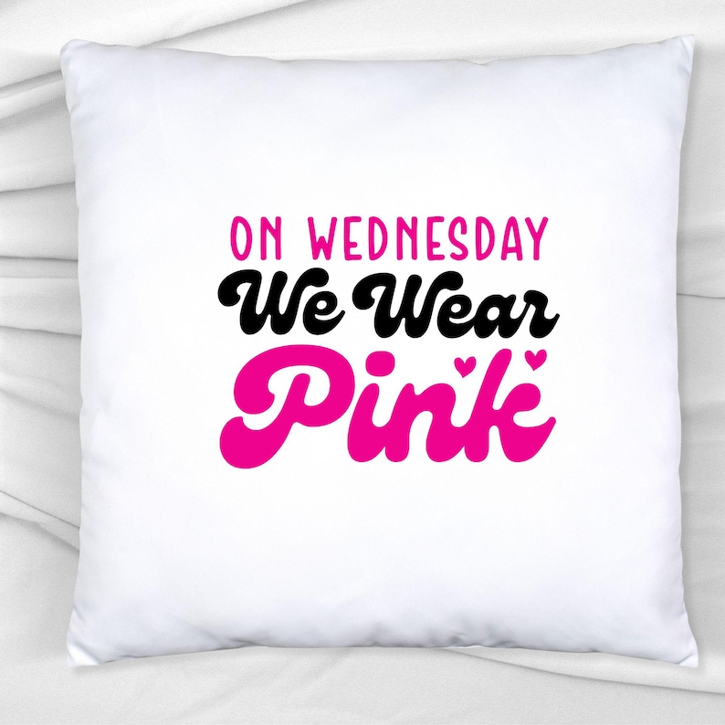 Pu&ograve; includere: Cuscino quadrato bianco con la scritta "ON WEDNESDAY We Wear Pink" in lettere nere e rosa. Il testo rosa include piccoli cuori. Il cuscino &egrave; su una superficie bianca.