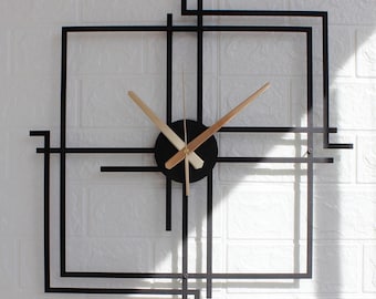 May include: A modern, geometric wall clock with a black frame and a circular black clock face. The clock hands are light brown. The clock is mounted on a white brick wall. The overall design is minimalist and contemporary.
