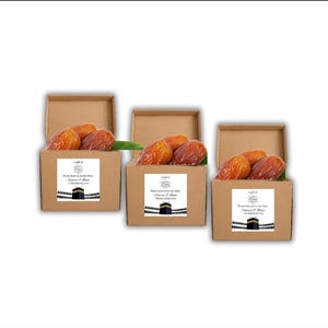 May include: Three open cardboard boxes filled with dates. Each box has a white label with text and a black and white illustration of a building. The dates are brown and arranged on a green leaf.