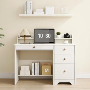 May include: A white desk with a drawer and three stacked drawers on the right. A laptop displays the time 10:30. A small lamp, books, and a camera are on the desk. A shelf above holds books and decorative items.