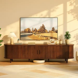 May include: A dark brown wooden TV stand with a curved design and vertical grooved detailing. The stand has two doors and sits on short, angled legs. A large flat-screen TV displays a landscape scene.