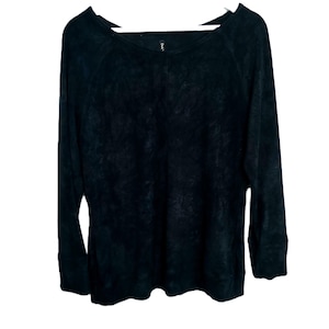 Puede incluir: Una camiseta negra de manga larga con cuello redondo. La parte superior tiene un aspecto texturizado y está colgada de una percha blanca. Las mangas son largas y el material parece suave. La parte superior es de color negro liso.