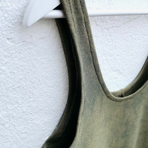 May include: A green sleeveless tank top with a scoop neck, hanging on a white hanger against a white wall.