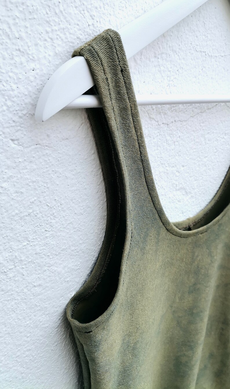 May include: A green sleeveless tank top with a scoop neck, hanging on a white hanger against a white wall.