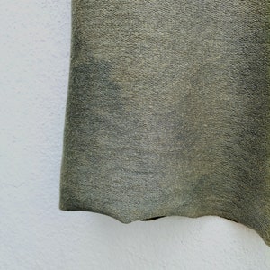 May include: Close-up of a dark green fabric with a textured surface. The fabric has a slightly wavy edge.