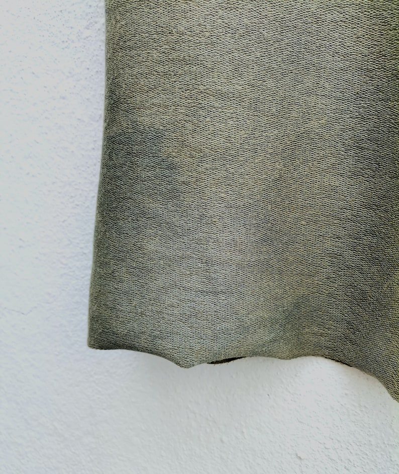 May include: Close-up of a dark green fabric with a textured surface. The fabric has a slightly wavy edge.