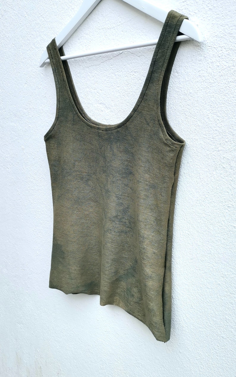 May include: A green sleeveless tank top with a tie-dye pattern. The tank top is hanging on a white hanger against a white wall.
