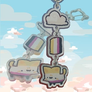 以下が含まれることがあります： 雲のチャーム、黄色、白、紫のカラーリングのチャーム2つ、カートゥーンの猫のデザインのチャーム2つが付いたキーホルダー。猫のチャームは黄色、白、紫のカラーリングです。