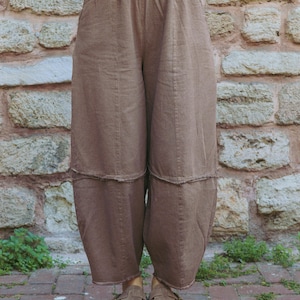 Könnte beinhalten: Braune Hose mit weitem Bein, elastischem Bund, vertikalen Nähten und einer horizontalen Naht im Oberschenkelbereich. Die Hose hat eine lockere Passform mit offen verarbeiteten Saumkanten an den Beinabschlüssen.