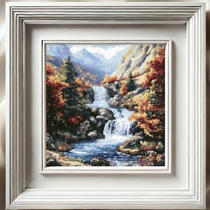Peut inclure: Paysage au point de croix encadré représentant une cascade dévalant une colline rocheuse. La scène présente une palette de couleurs automnales, avec des rouges, des oranges et des jaunes, des arbres à feuilles persistantes et un ciel bleu. L'œuvre est encadrée dans un cadre blanc carré.