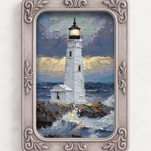 May include: A framed cross-stitch of a lighthouse on a rocky shore. The white lighthouse has a lit lamp at the top, set against a stormy sky and ocean. The frame is a light gray with ornate detailing.