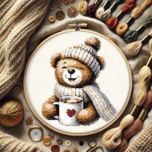 May include: A brown teddy bear wearing a white and brown knitted hat and scarf, holding a white mug with a red heart on it. The bear is sitting on a white background.