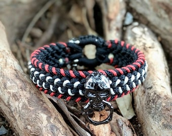 May include: A black, red, and white braided bracelet with a silver skull charm. The bracelet is made with paracord and has a simple knot design.