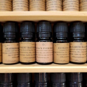 May include: A shelf of small brown glass bottles with black caps, each labeled with a different essential oil blend. The labels include names like "Forest Bathing", "Joi Blend", and "Earth Blend".
