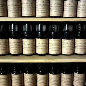May include: A shelf with three rows of small brown glass bottles with black caps. Each bottle has a label with a different name and description of an essential oil blend. The labels are all in a vintage style font and have a brown background.