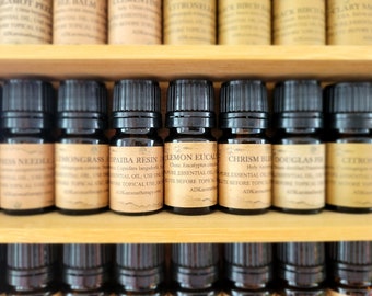 May include: A wooden shelf with rows of small brown glass bottles with black caps. Each bottle has a label with a different essential oil name and description. The labels are printed in a vintage style font. The oils include Lemongrass, Copaiba Resin, Lemon Eucalyptus, and Douglas Fir.
